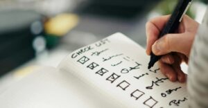 uma mão sobre um papel com uma lista com marcações de realizado